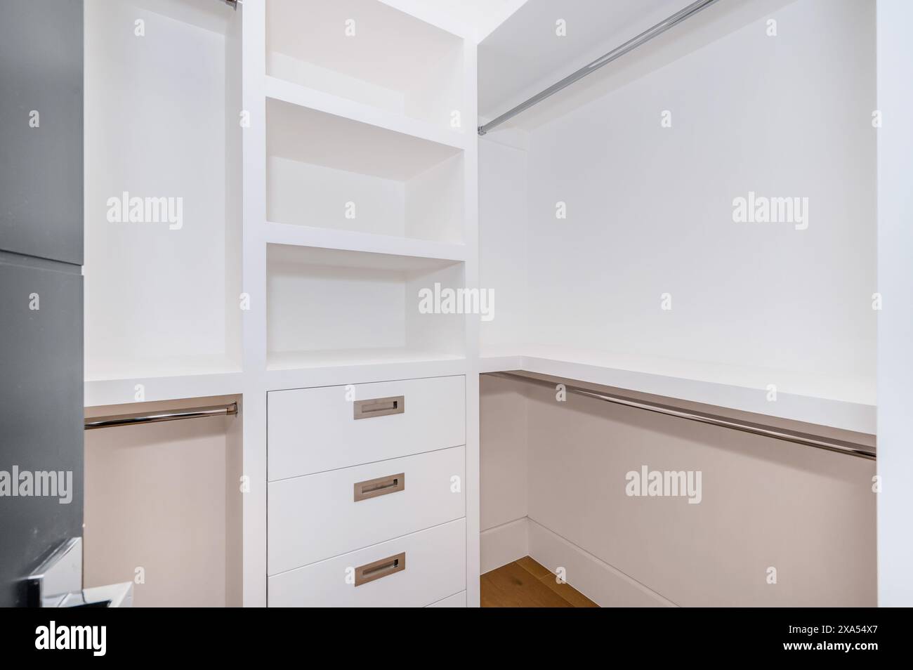 A spacious walk-in closet featuring elegant wooden floors and pristine white walls Stock Photo