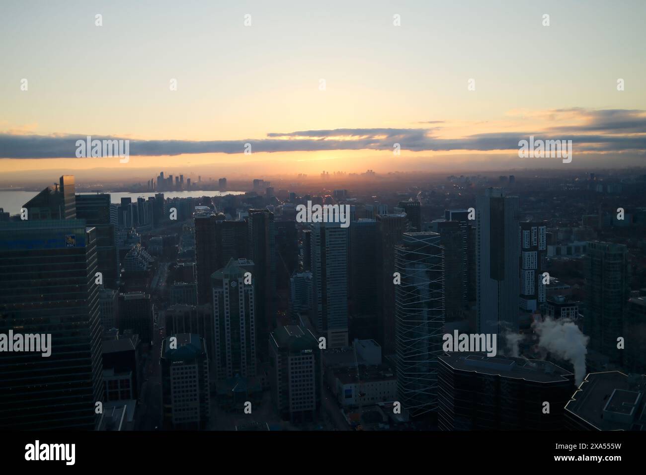 An urban skyline at sunset reflecting on water with cloudy orange sky ...