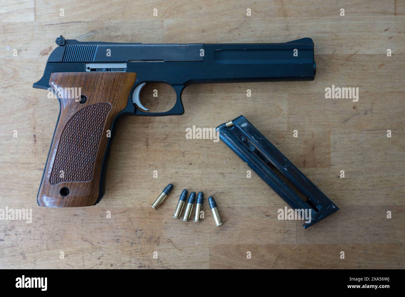 A nice classic .22 caliber pistol, a loaded magazine and a few standard bullets on the wooden table Stock Photo