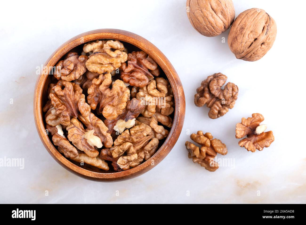 Walnut halves in a wooden bowl on a marble plate. Shelled and dried kernels, ripe seeds of the common walnut tree Juglans regia. Stock Photo
