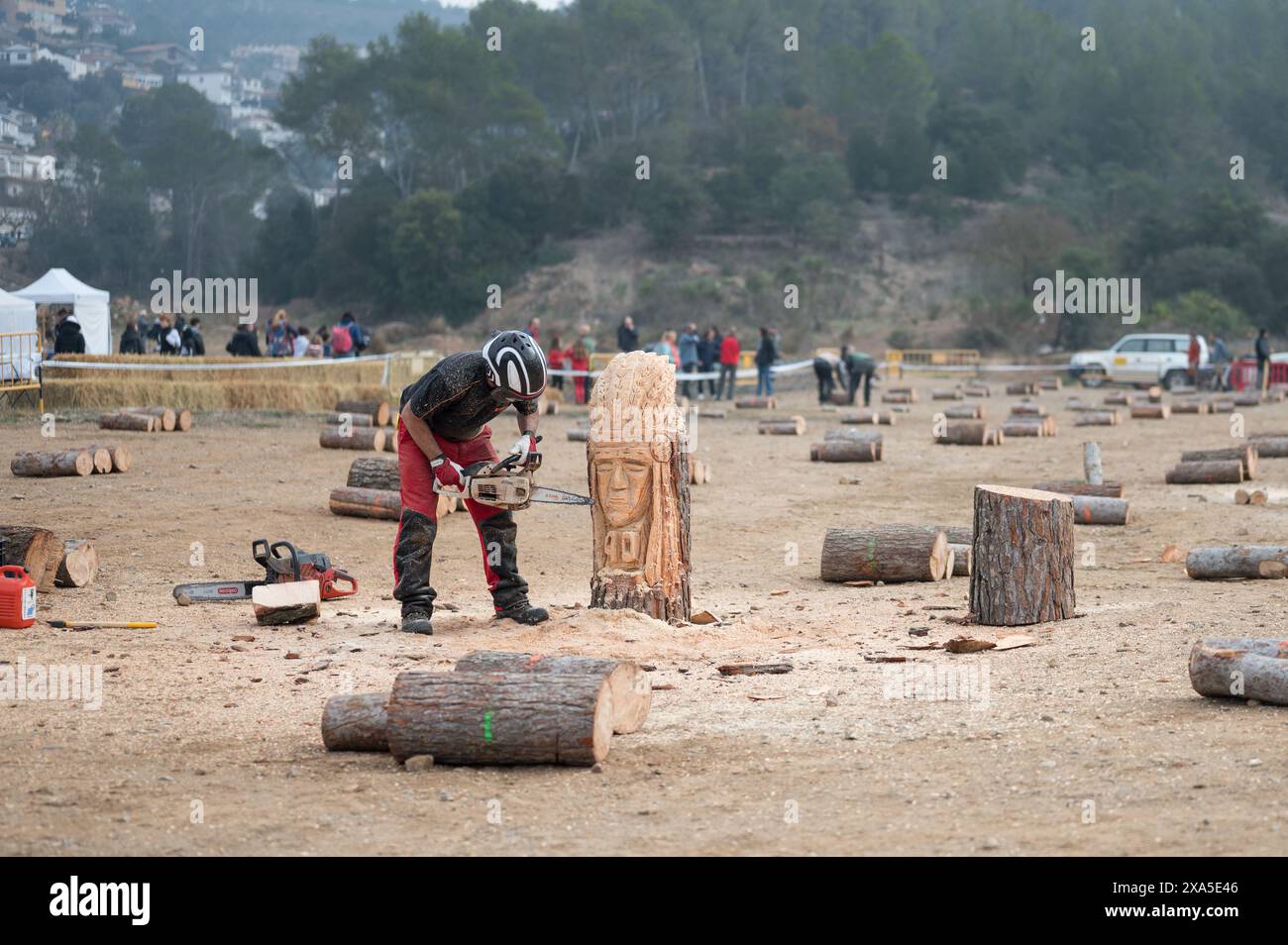 Detail of a crouching sculptor sculpting a tree trunk with a chainsaw. These are the festivals of the town Torrelles de Llobregat. It's a foggy day. Stock Photo