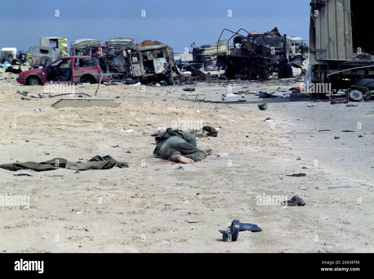 5th March 1991 The body of a soldier lies in the desert with an assortment of destroyed military and civilian vehicles of an Iraqi military convoy forming a backdrop. It was attacked on Route 801, the road to Um Qasr, north of Kuwait City, by the American air force as the Iraqi army was attempting to flee to Iraq. Stock Photo
