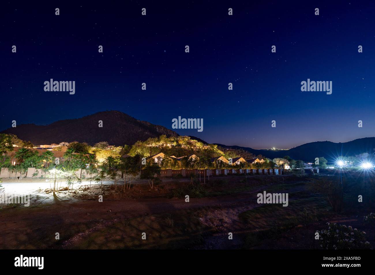 The city lights illuminate night sky with trees and hill silhouette Stock Photo