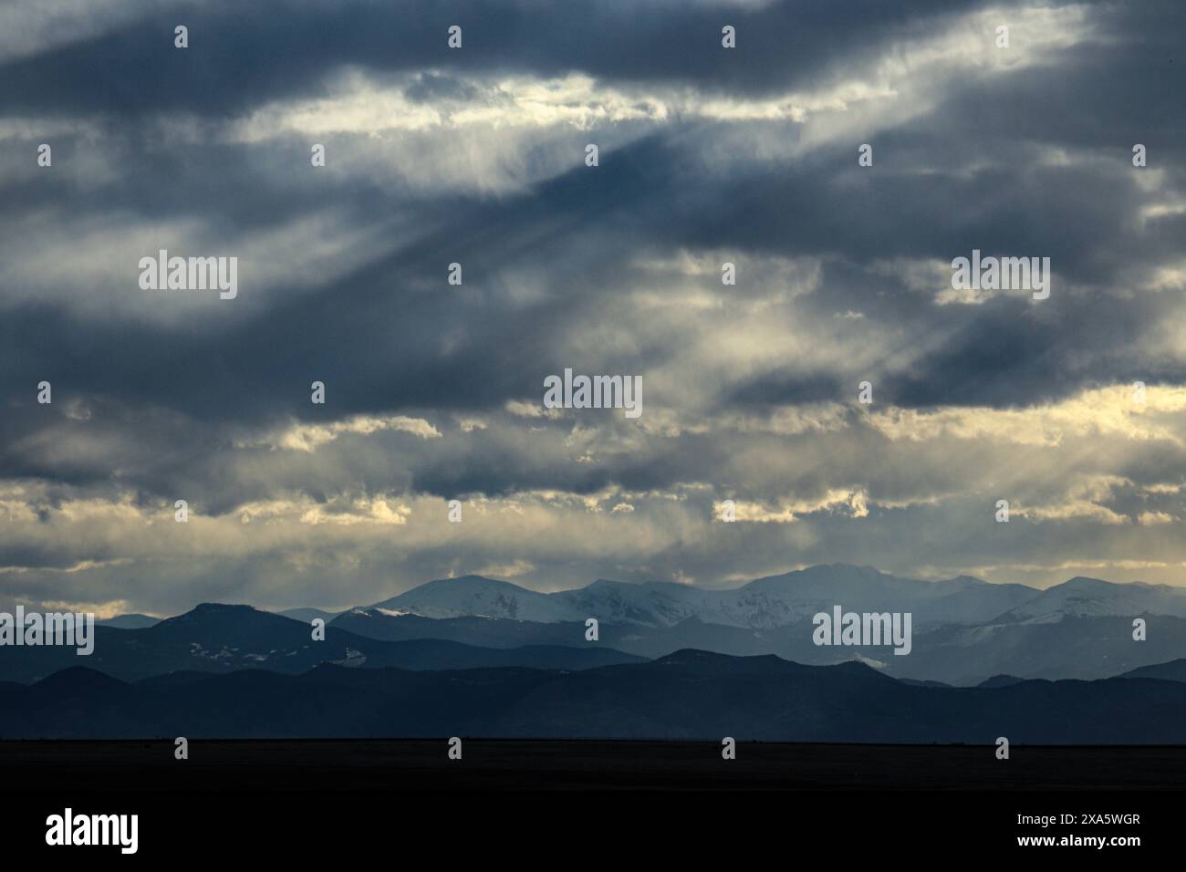 The mountains under a cloudy sky with sun rays peeking through dark clouds. Stock Photo