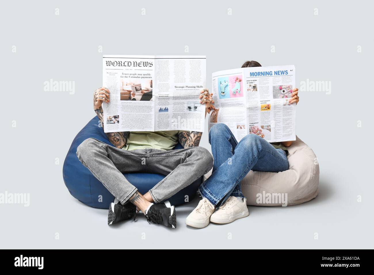 Couple in beanbag chairs with newspapers on grey background Stock Photo