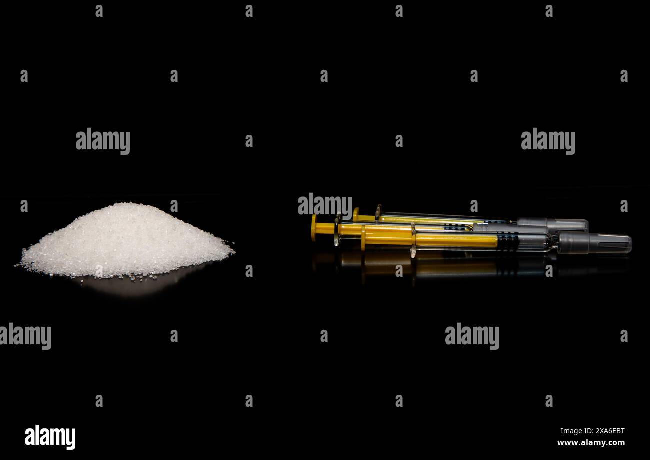 A pile of crystallized white powder and a few syringes on a black background Stock Photo