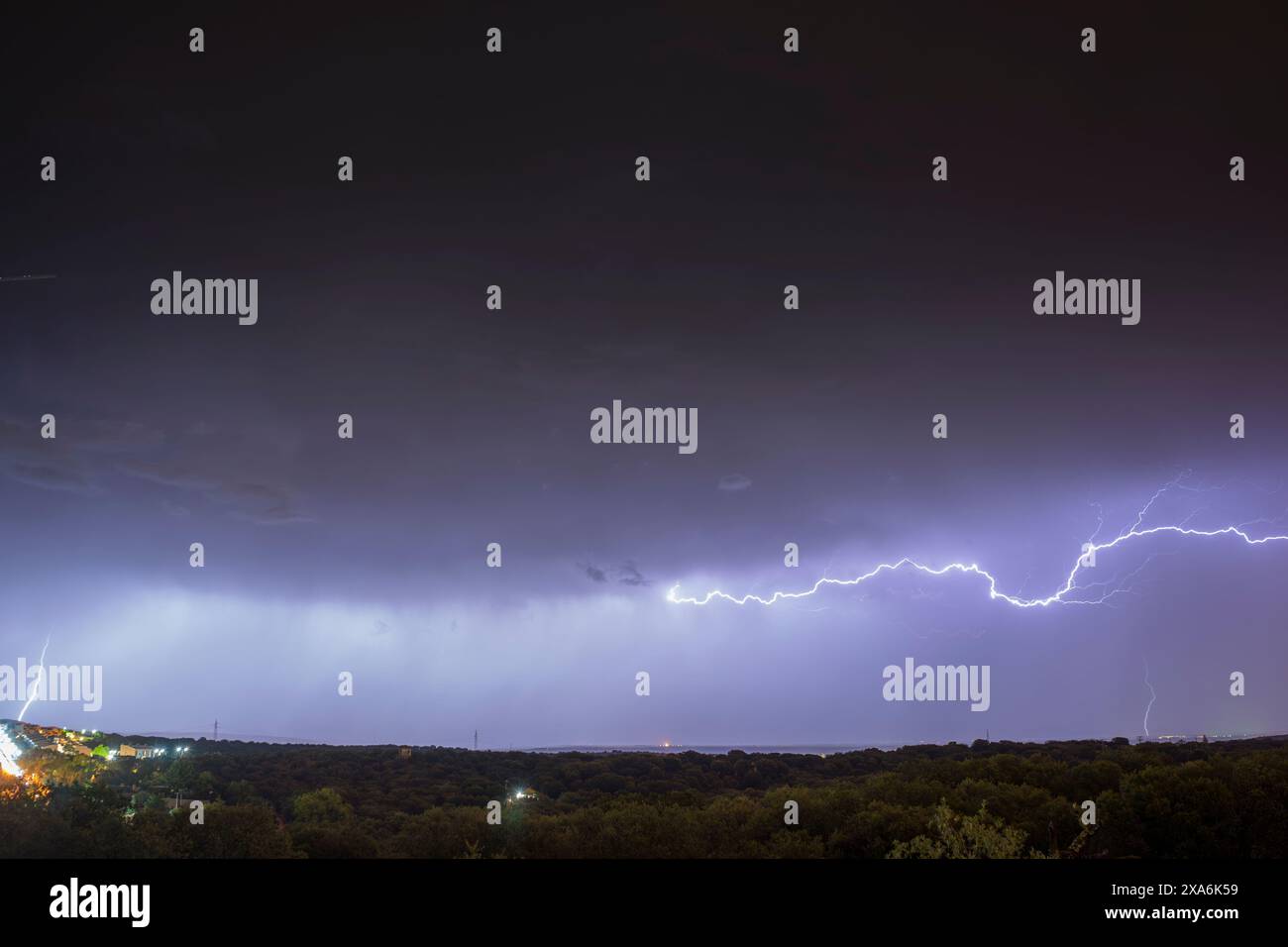 A spectacular night storm dominates the sky, marked by significant lightning, while on the horizon the lights of the big cities illuminate. Stock Photo