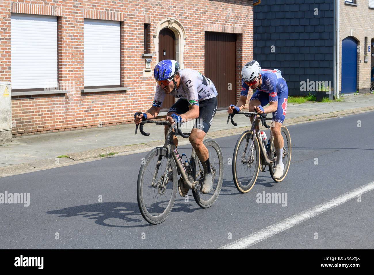 Two cyclists ride past a brick building on a city street Stock Photo