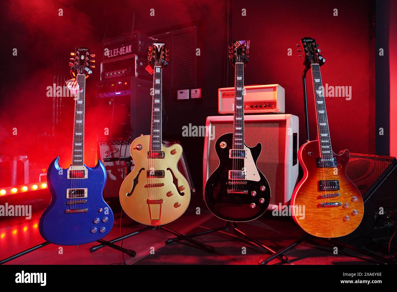 The four electric guitars displayed on stands in front of an amplifier and other music equipment Stock Photo