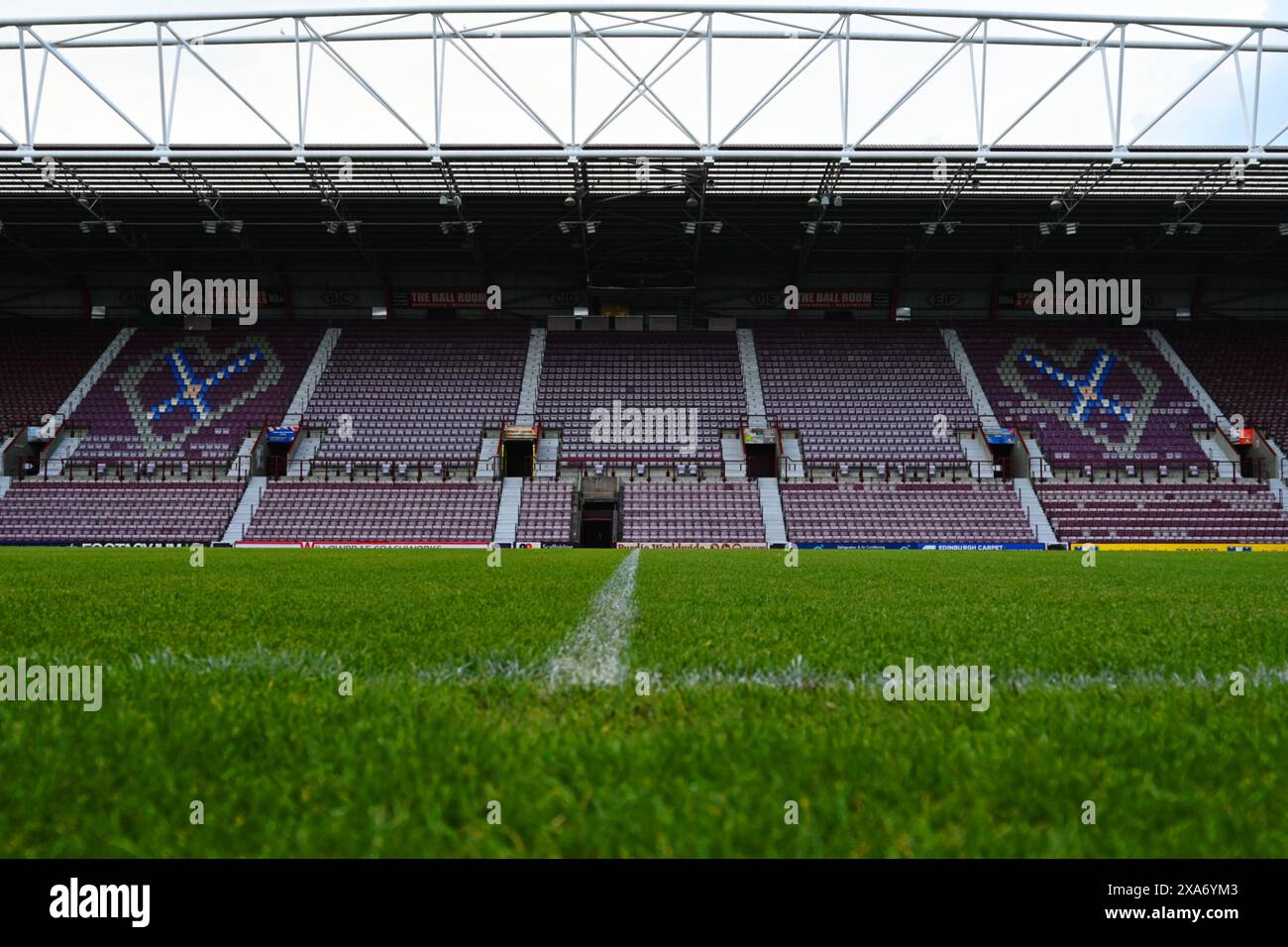 A deserted soccer stadium with green field, empty seats, and a clock above Stock Photo
