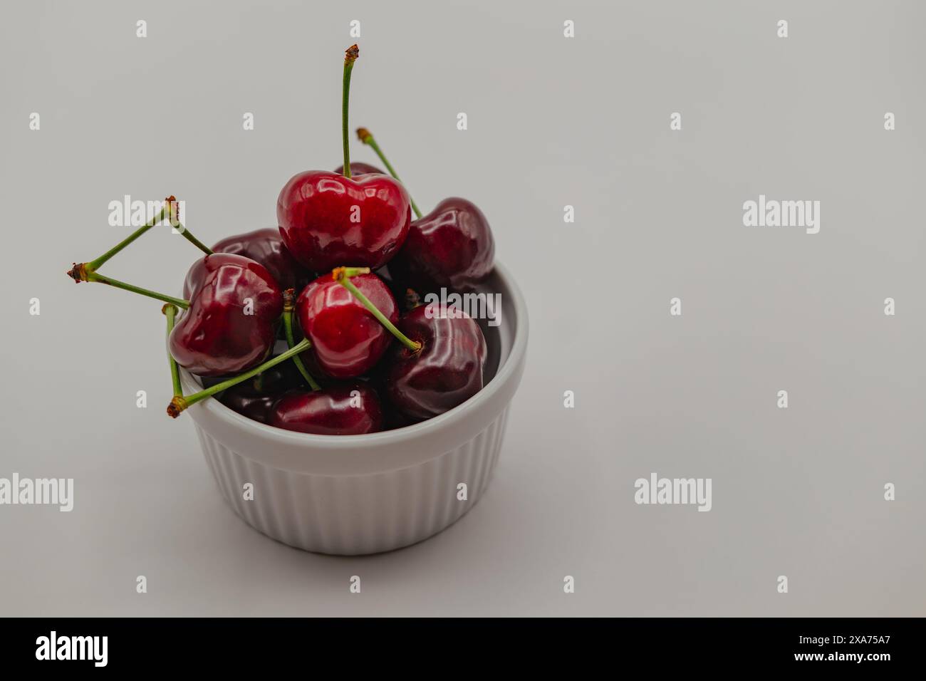 A closeup shot of fresh cherries in a bowl on white tablecloth Stock Photo