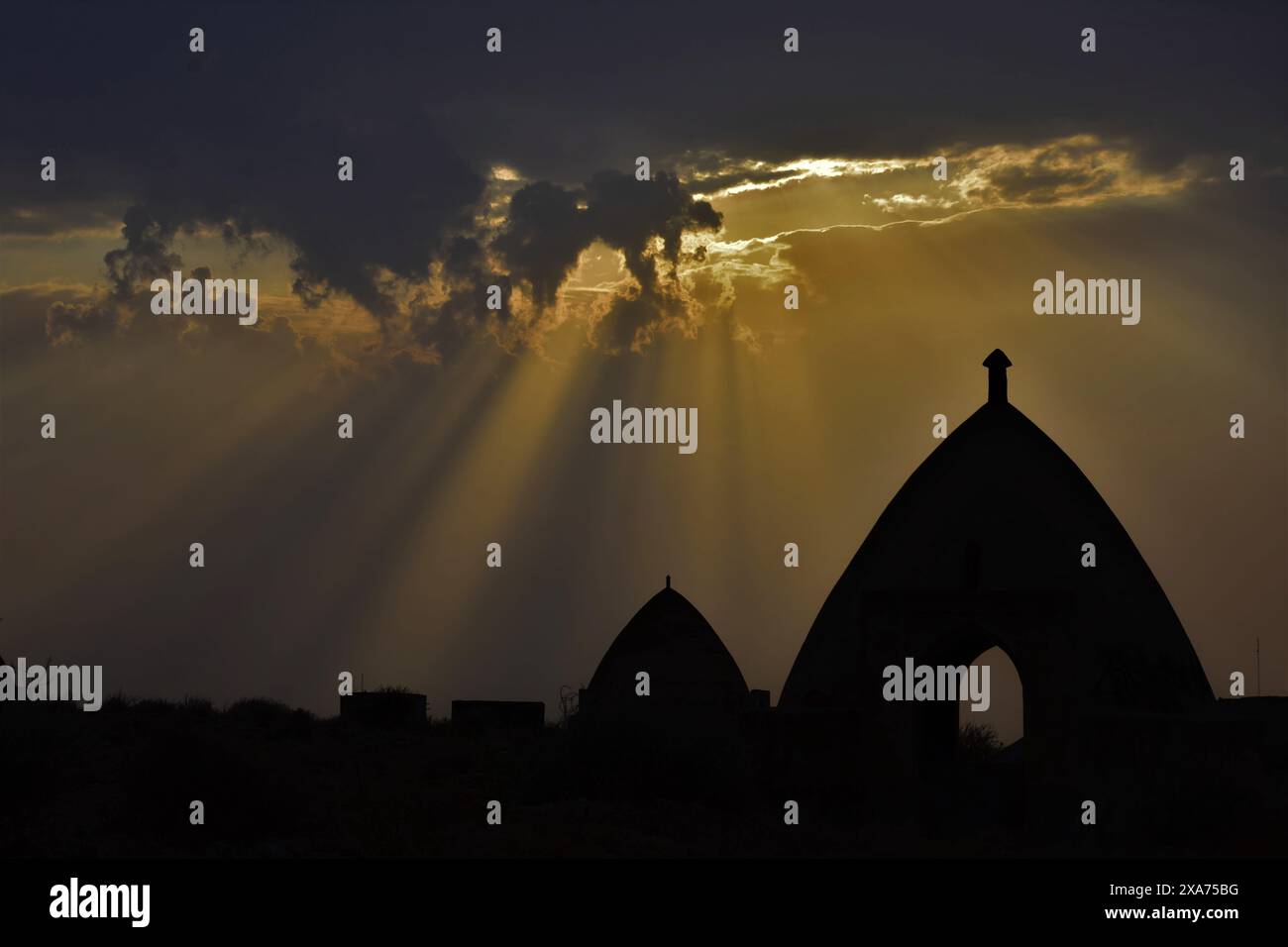 Sun rays shining through clouds in a silhouette image during sunset Stock Photo