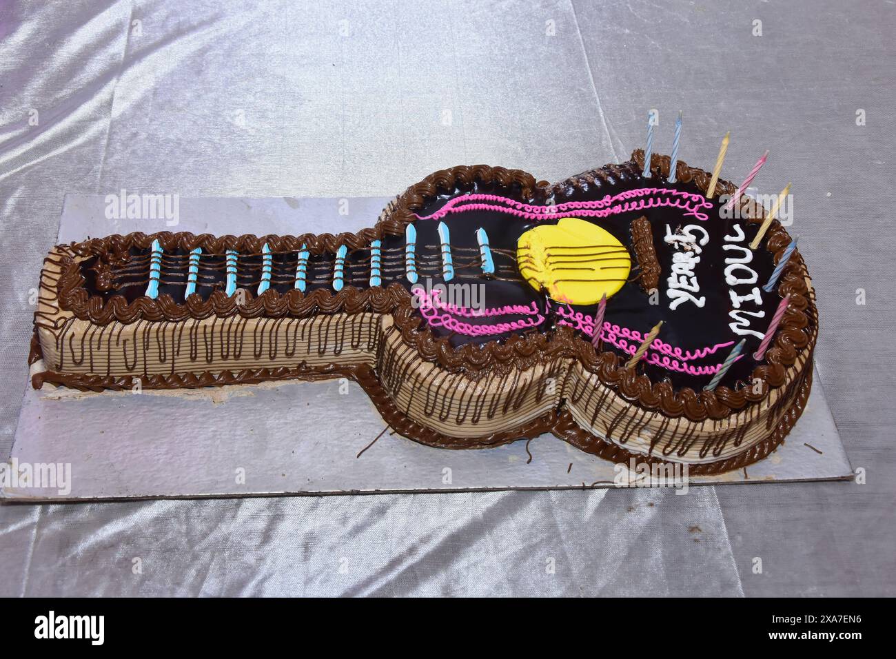 A guitar-shaped birthday cake with decorative elements on a reflective ...