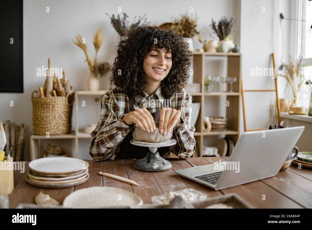 Woman shaping pottery while using laptop in studio Stock Photo
