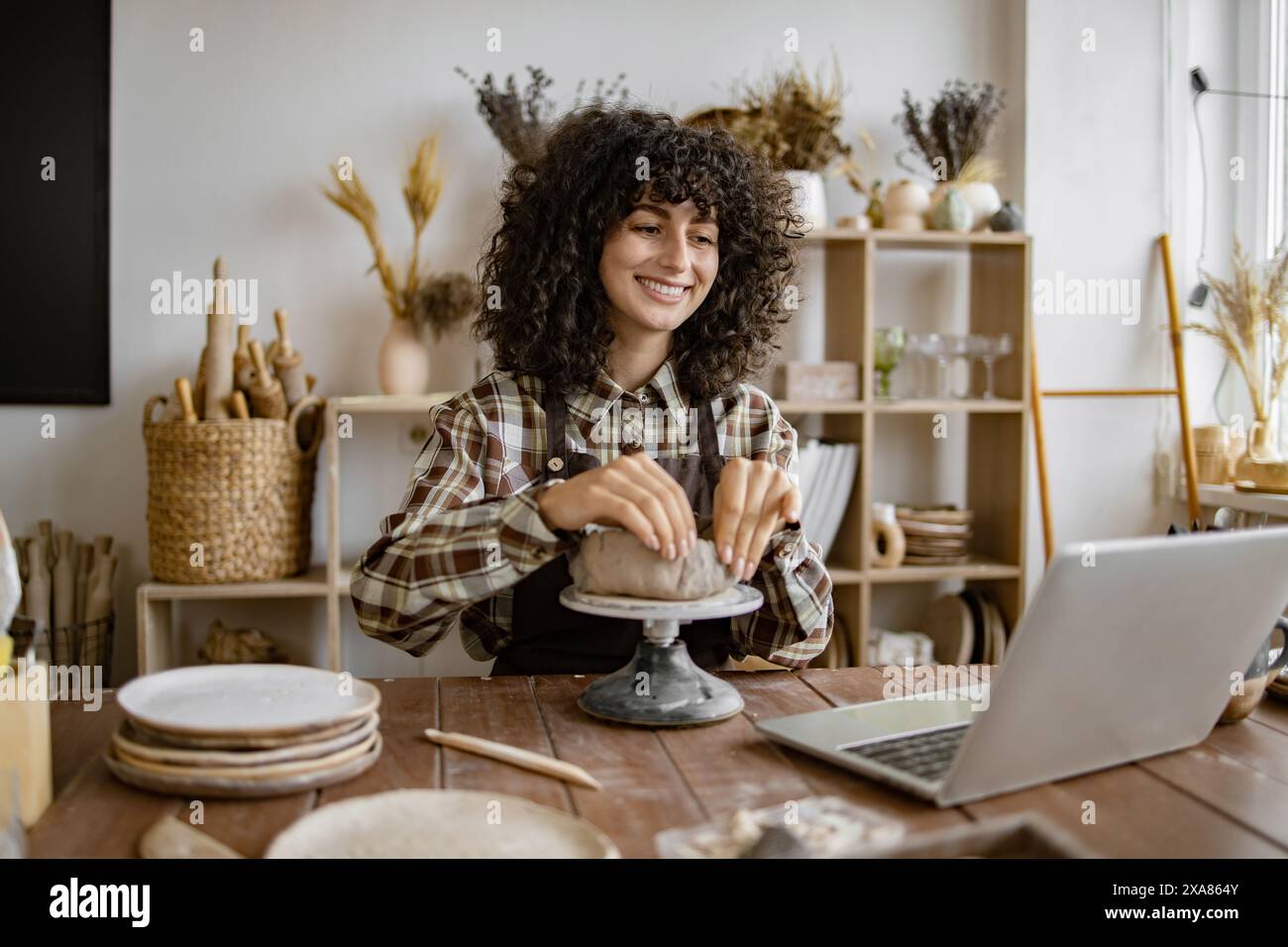 Woman working on pottery using laptop in ceramic studio Stock Photo