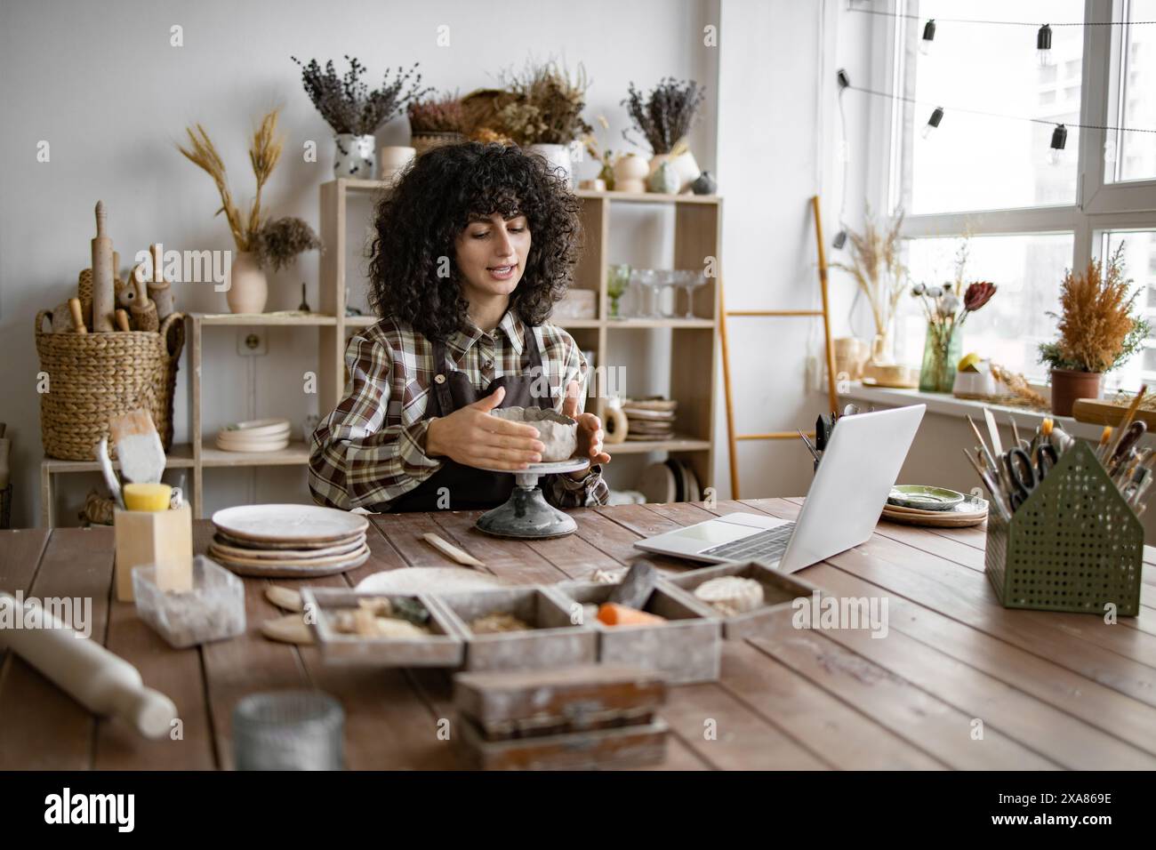 Young woman making pottery while using laptop in studio Stock Photo