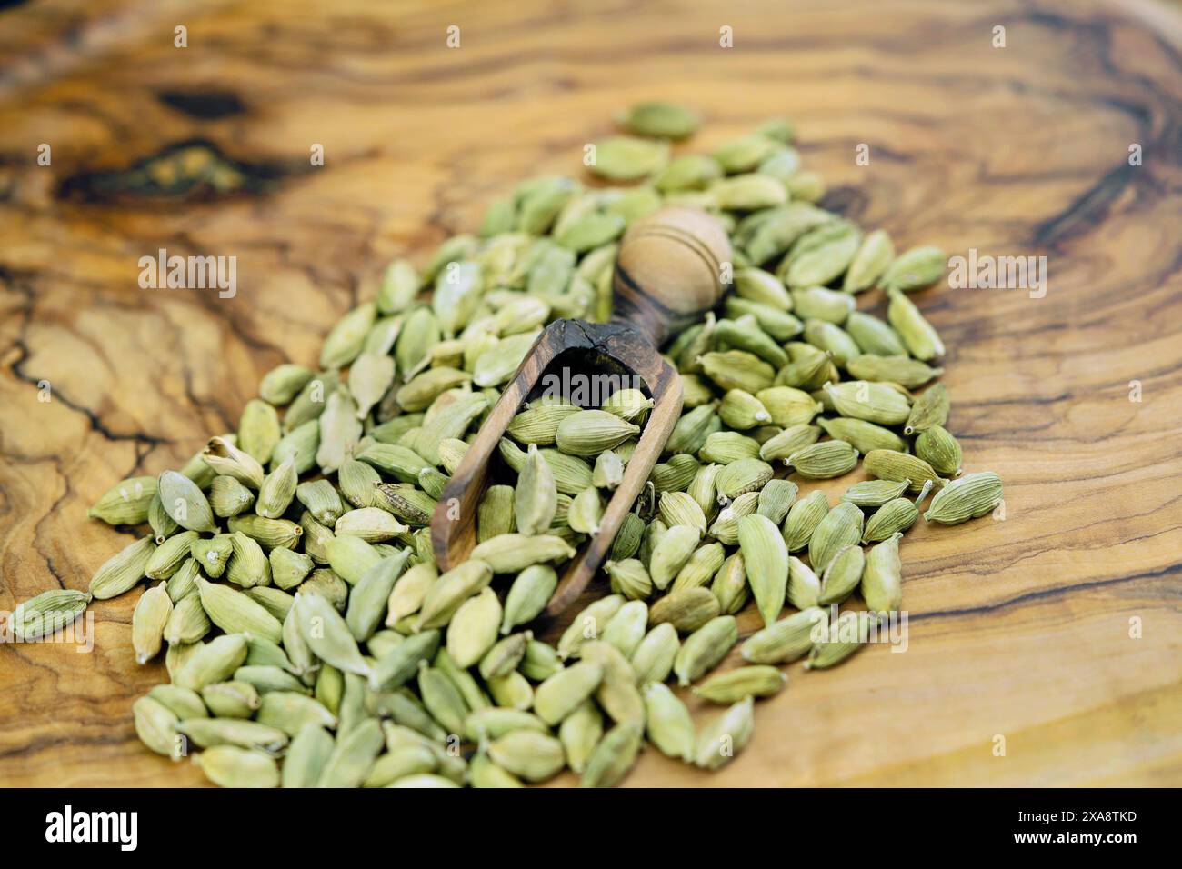 true cardamom (Elettaria cardamomum, Amomum cardamon), green cardamom on a wooden board with a wooden scoop Stock Photo