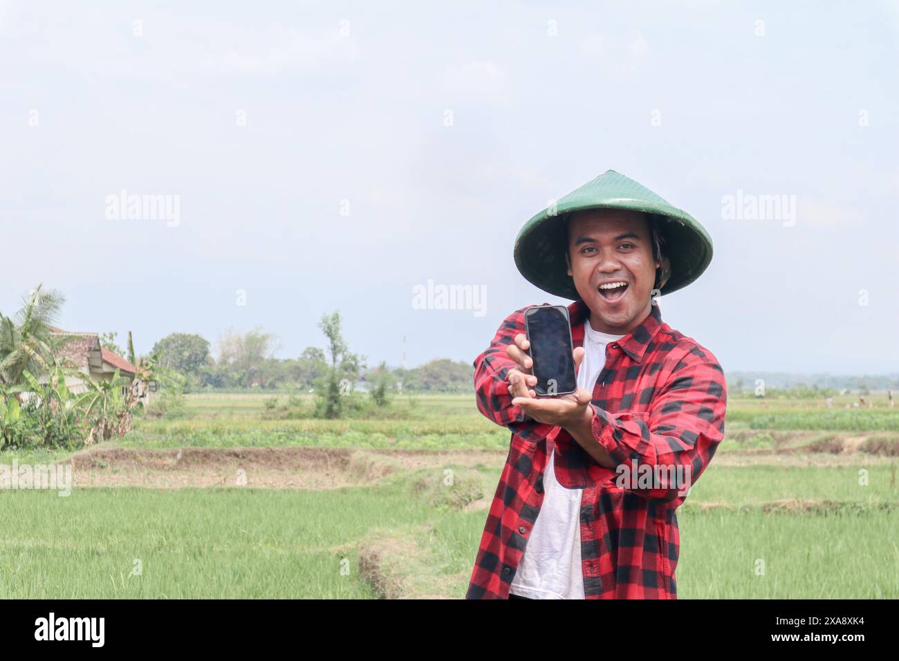 Portrait of a shocked Asian male farmer wearing a hat, holding his ...