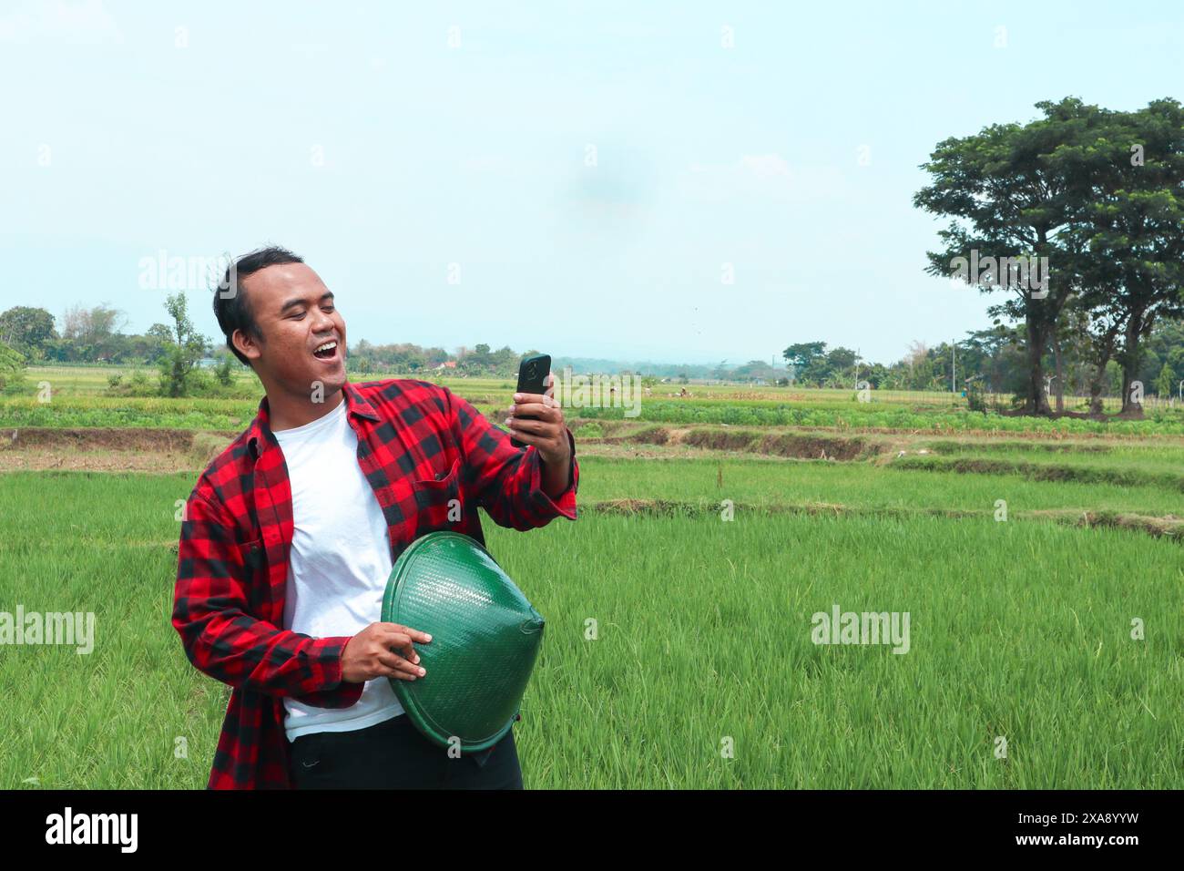 Portrait of a shocked Asian male farmer wearing a hat, holding his ...