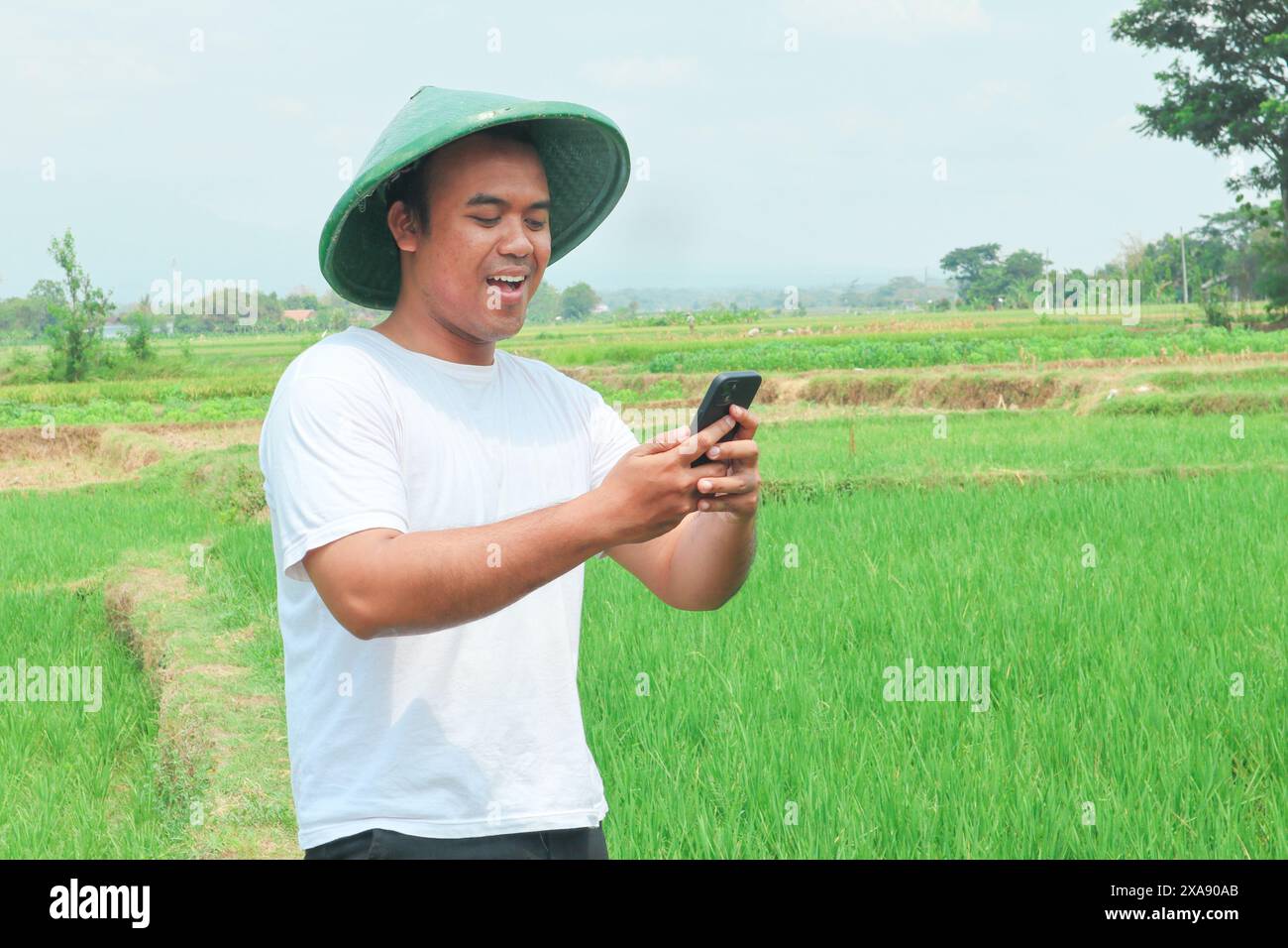 Portrait of a shocked Asian male farmer wearing a hat, holding his ...