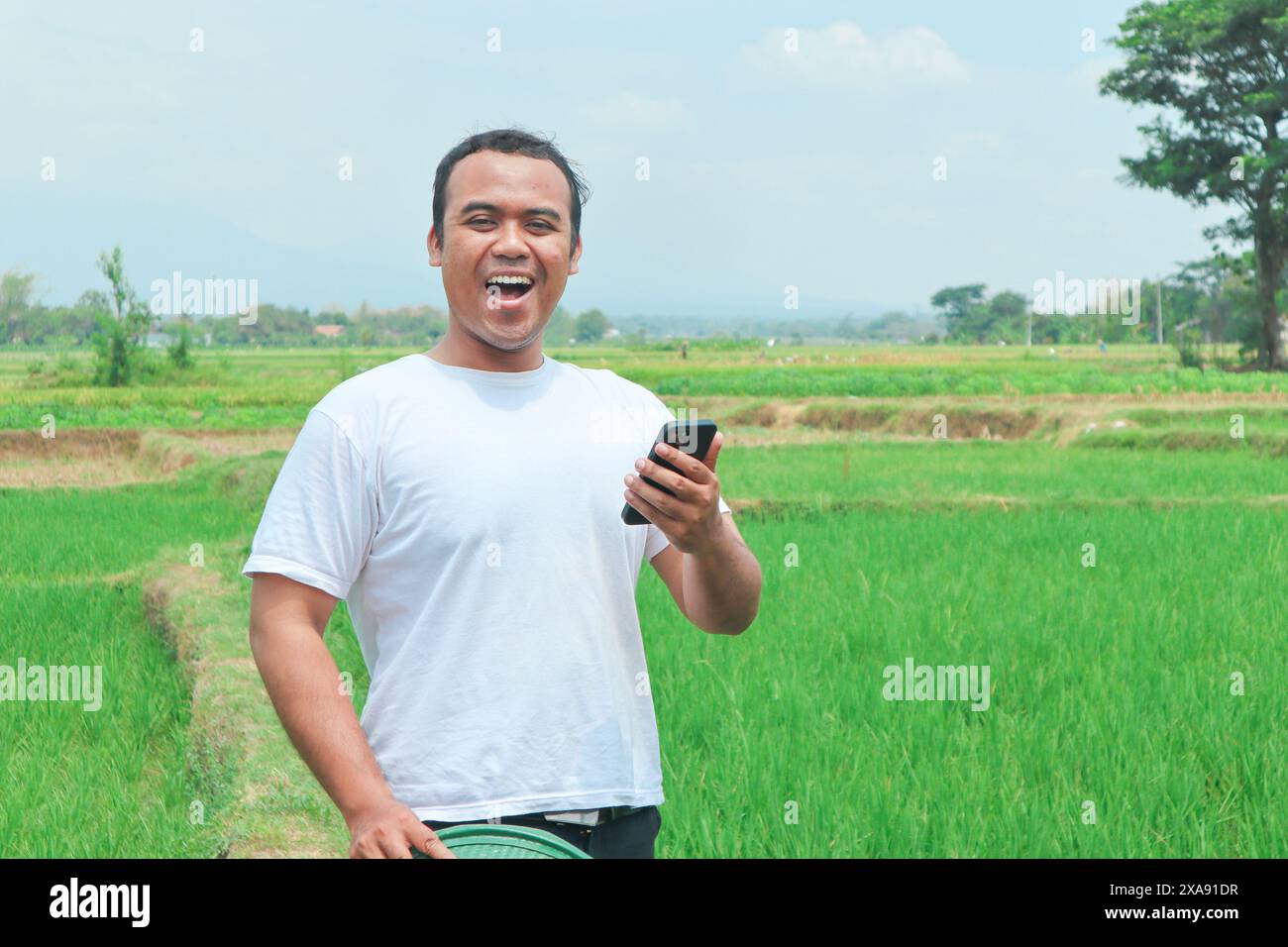Portrait of a shocked Asian male farmer wearing a hat, holding his ...