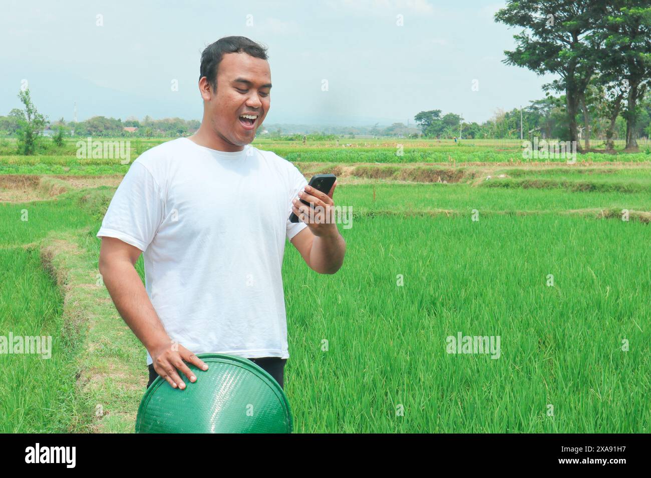Portrait of a shocked Asian male farmer wearing a hat, holding his ...