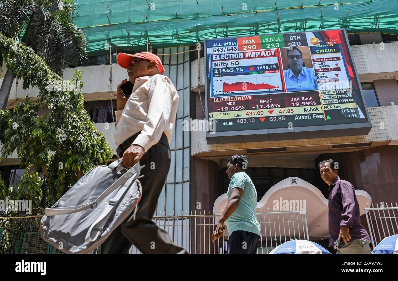 People walk past the Bombay Stock Exchange (BSE) building as the screen flashes the Loksabha election results and its impact on stock trading. The stock market was volatile when it opened in the morning due to election result, there was an anticipation of Bharatiya Janata Party (BJP) getting the majority of the votes and Prime Minister Narendra Modi getting elected for the third time, but that wasn't the case as opposition parties gave tough fight to the Bharatiya Janata Party (BJP) as votes were being counted and result was flashed on the screen which impacted the stock trading heavily. Stock Photo