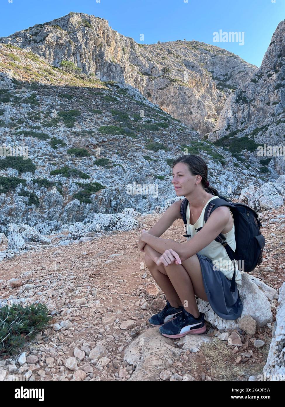 A woman hiker in mountains, kneeling on a rock, taking a rest in Greece ...