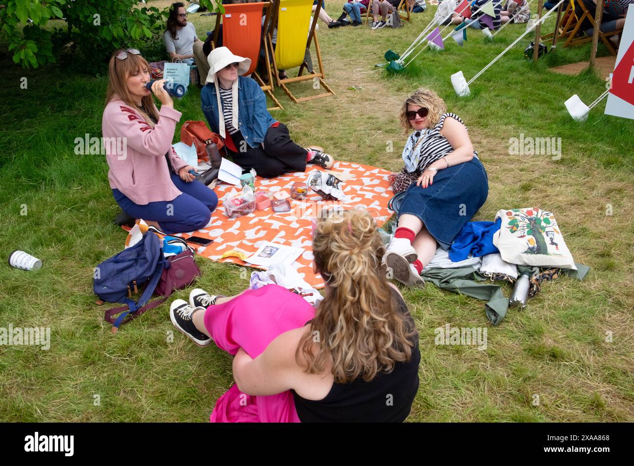 Women friends relaxing on the lawn grass outside in the Hay Festival garden site reading books 2024 Hay-on-Wye Wales UK Great Britain  KATHY DEWITT Stock Photo