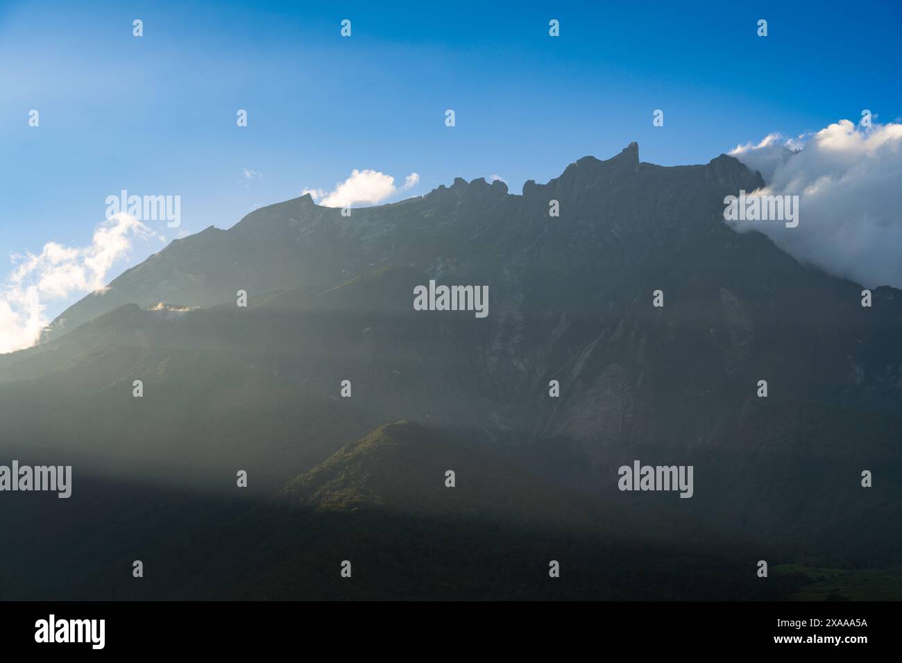 Mountain shrouded in clouds and grass under blue sky Stock Photo - Alamy