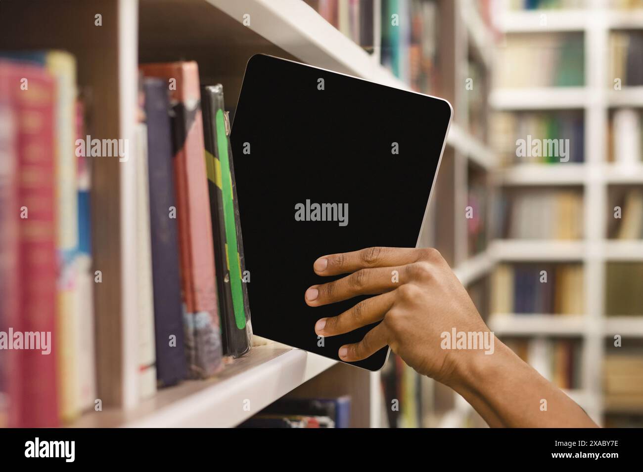 Afro student placing digital tablet on bookshelf Stock Photo