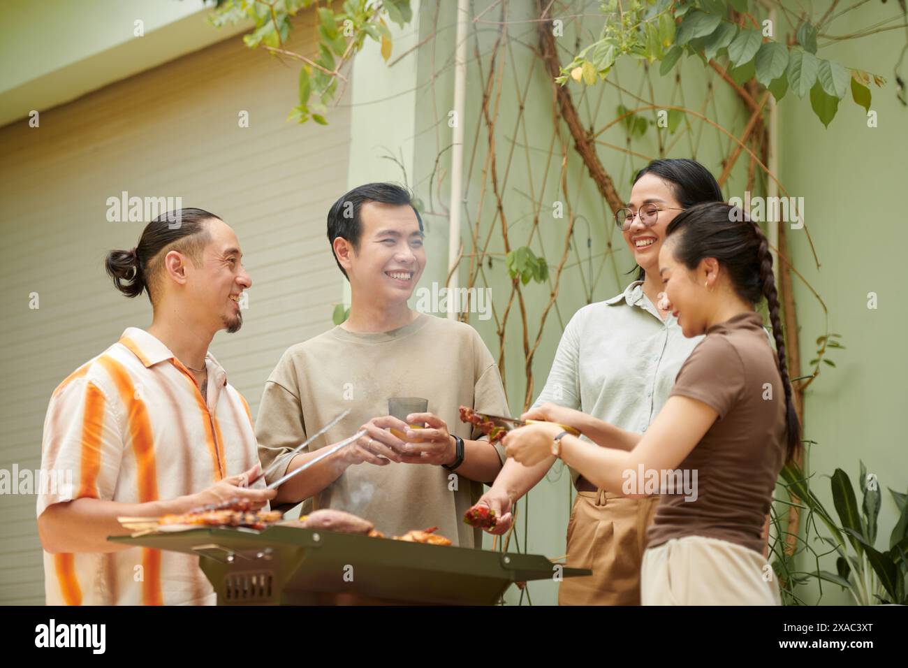 Joyful friends chatting and joking around when having barbeque in backyard Stock Photo