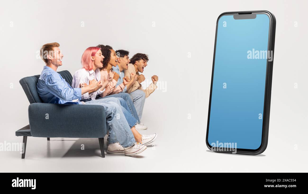 Multiracial group sitting on couch, looking at huge phone Stock Photo