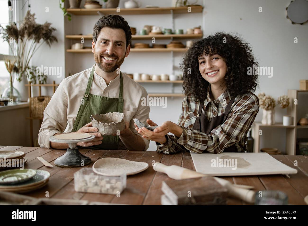 Smiling bearded man and woman sculpting clay vases and bowls in cozy ...