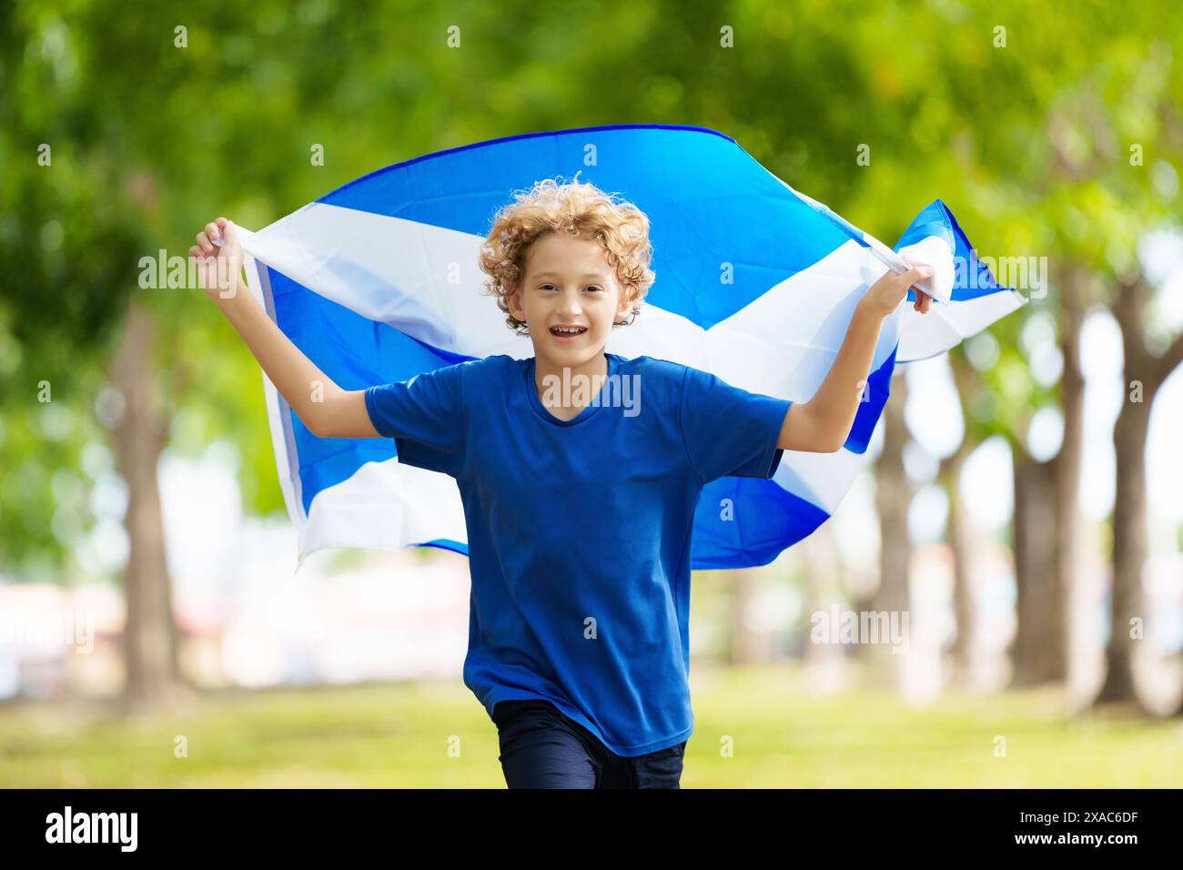 Child running with Scotland flag. Scotland football supporter kid. Scottish fan national jersey cheering for victory. Championship game. Go Scotland Stock Photo