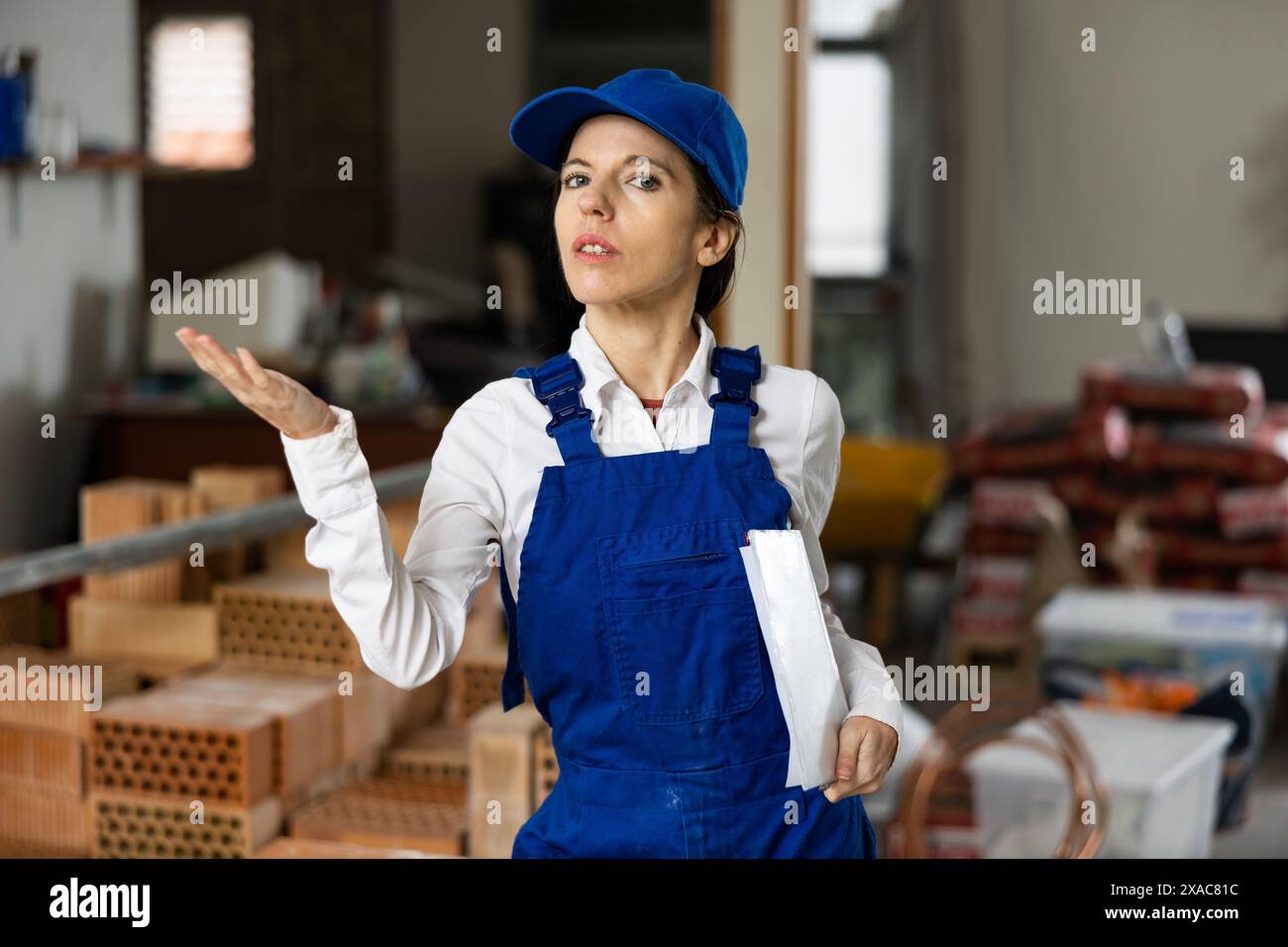 Female builder wearing overalls and cap posing at construction site, looking at camera Stock Photo