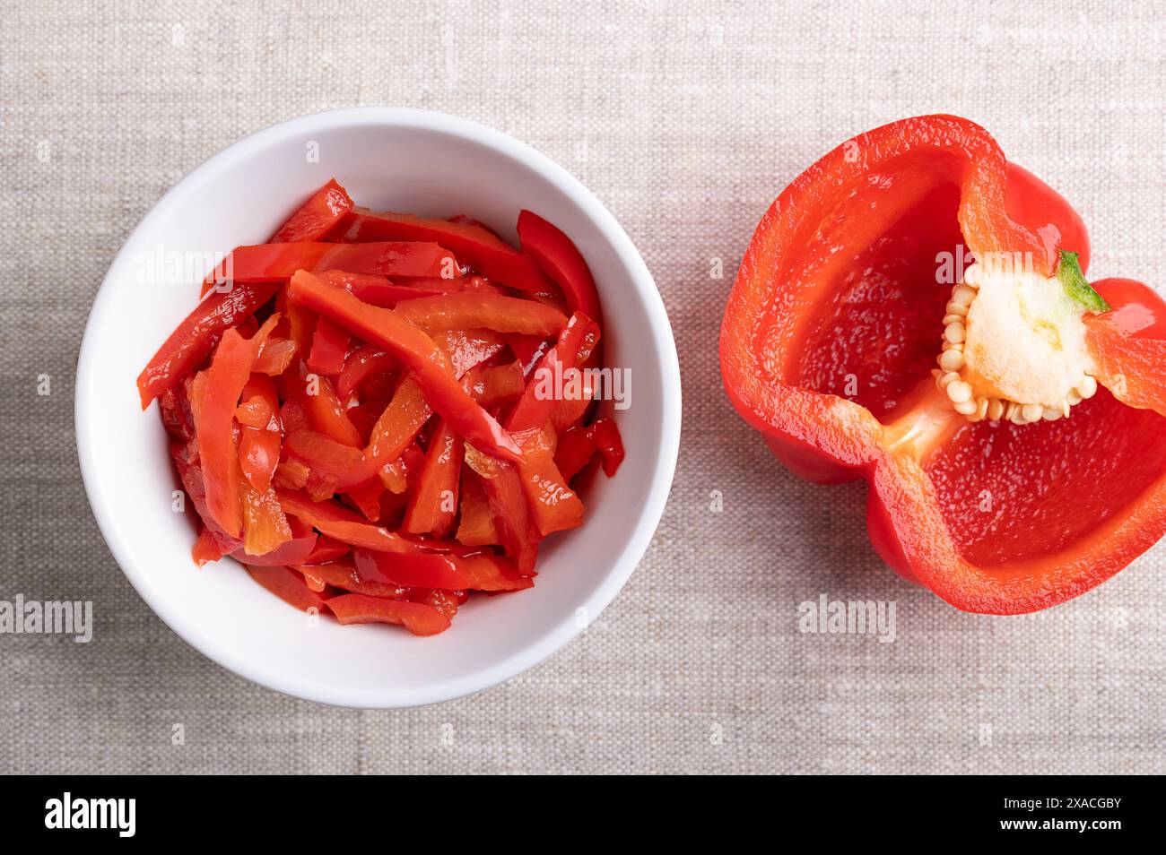 Red pepper salad, pickled red bell pepper strips in a white bowl on linen fabric. Paprika salad, made of sliced, sweet peppers. Stock Photo