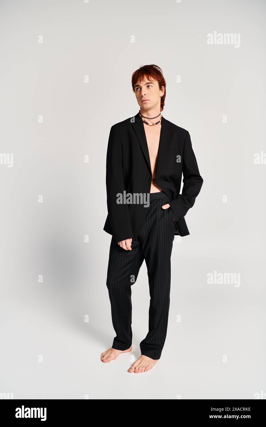 A stylish young man in a black suit confidently stands before a plain ...