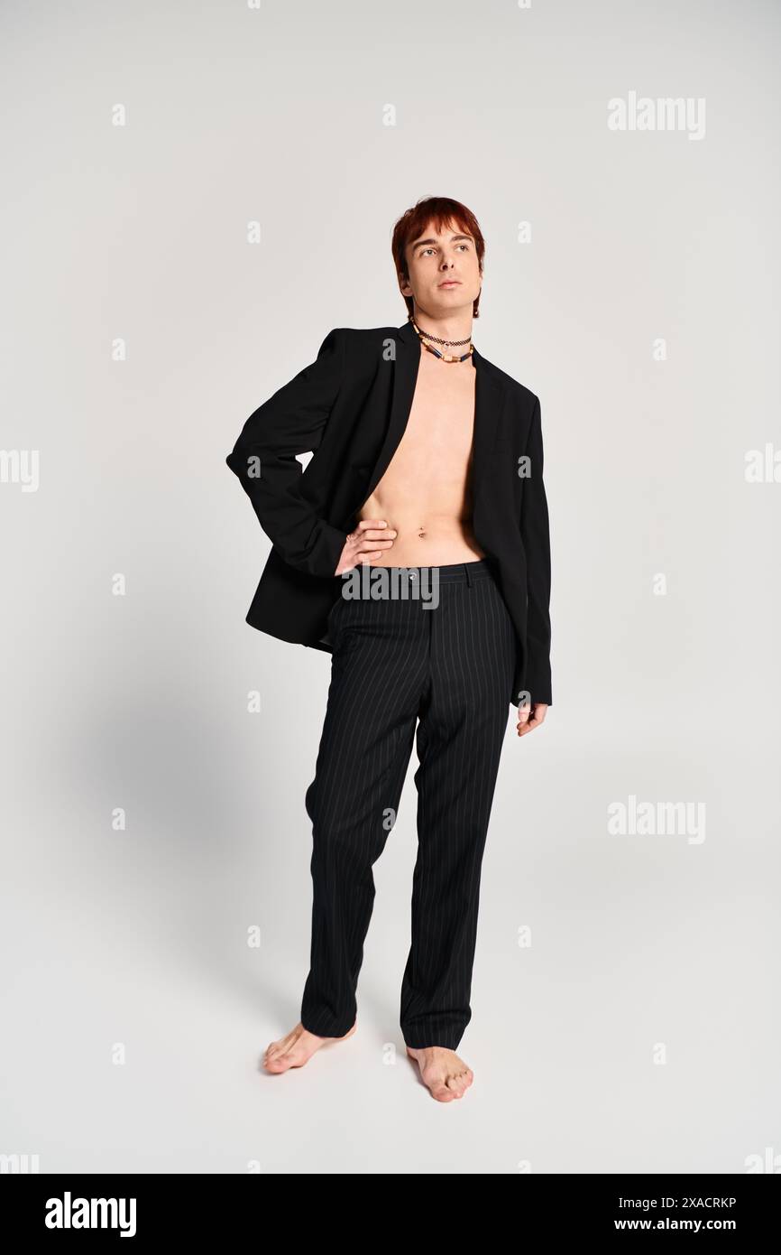 A stylish young man in a suit strikes a confident pose against a grey ...