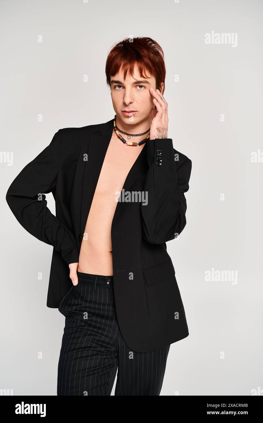A stylish young man in a suit strikes a pose in a studio with a grey ...