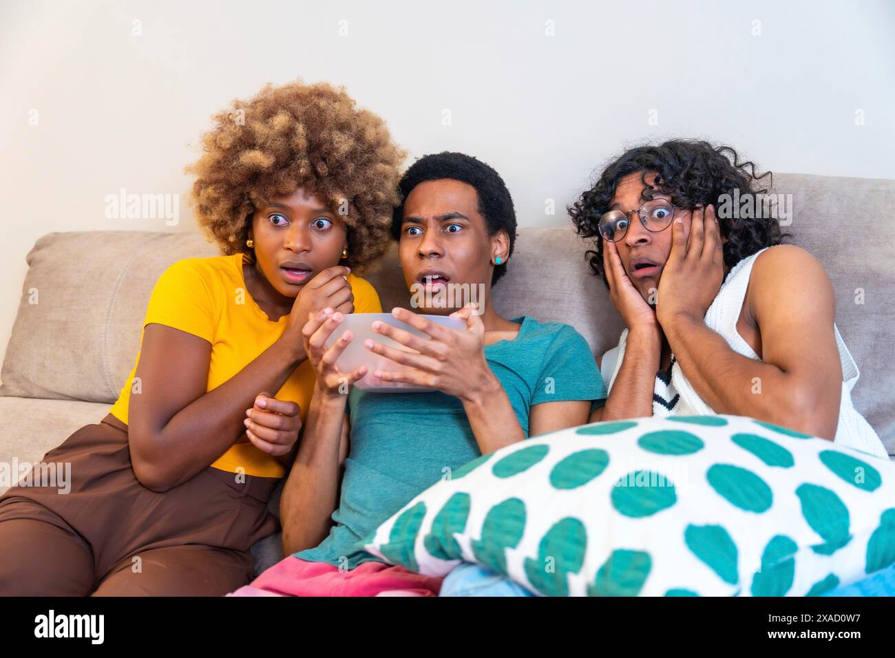 Multi-ethnic friends watching horror movie and eating pop corn sitting on the sofa at home Stock Photo