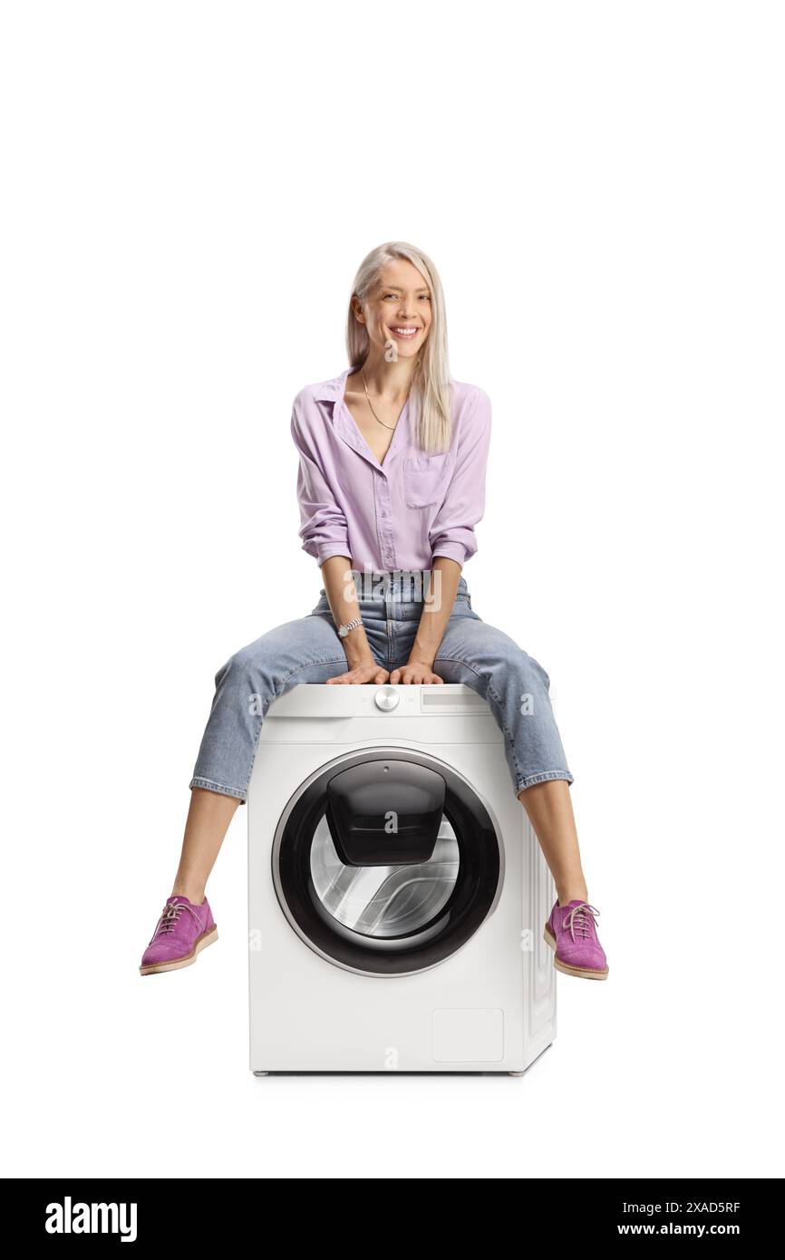 Smiling woman sitting on top of a washing machine isolated on white background Stock Photo