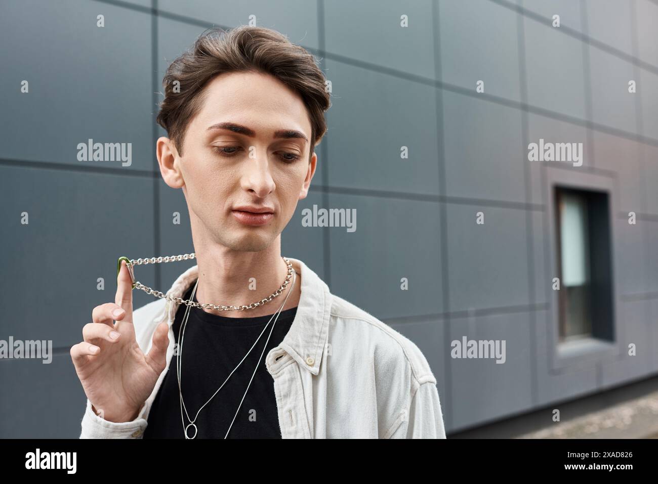 A stylish young individual holds a necklace in front of a majestic