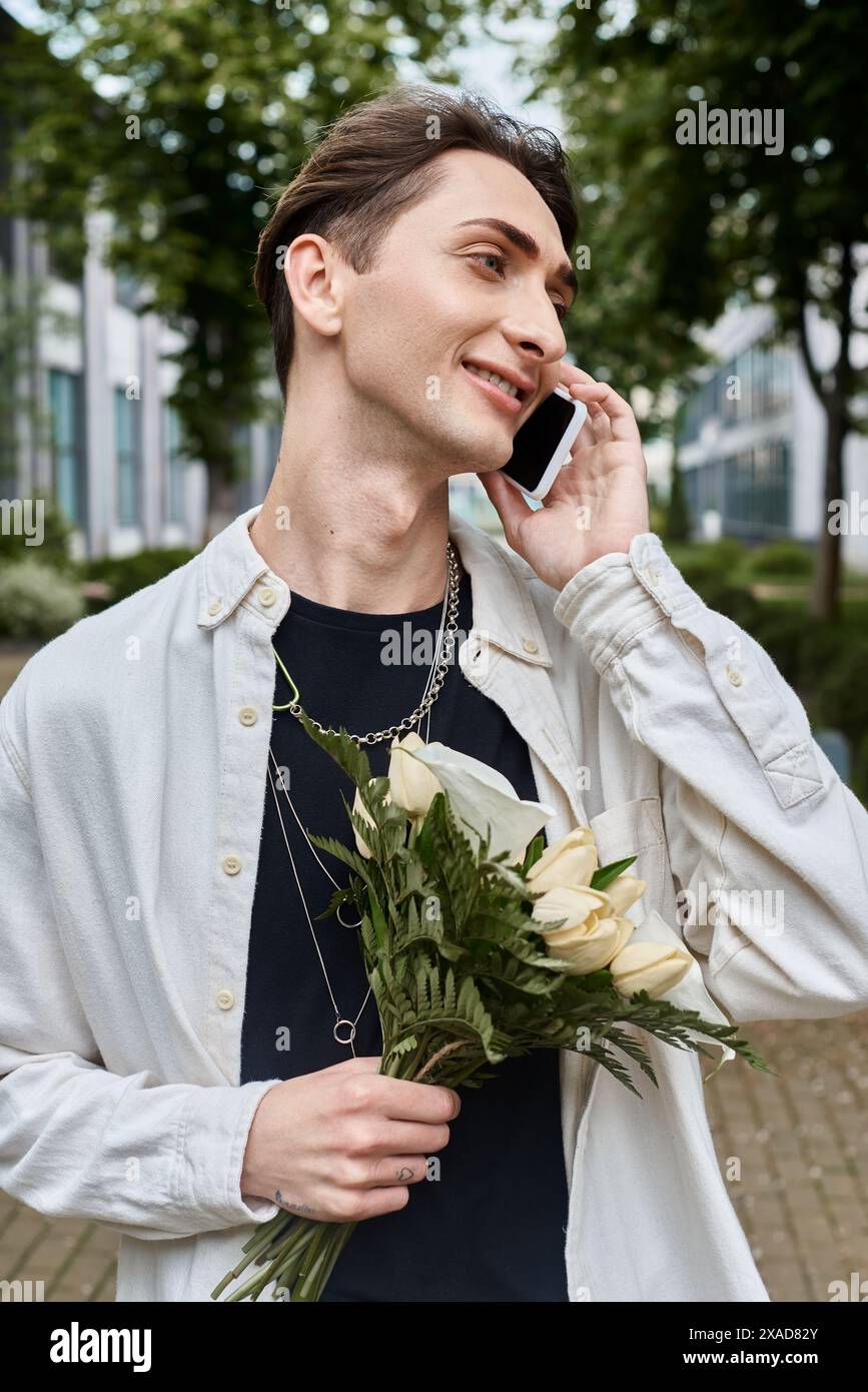 A young queer individual in stylish attire juggles holding a bouquet of flowers while talking on the phone. Stock Photo