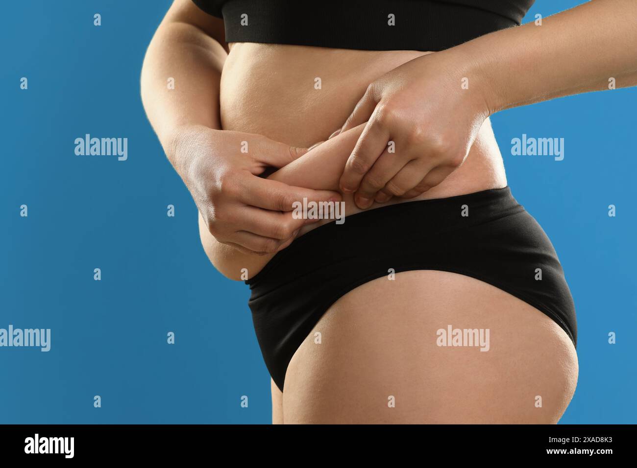 Woman touching belly fat on light blue background, closeup. Overweight problem Stock Photo