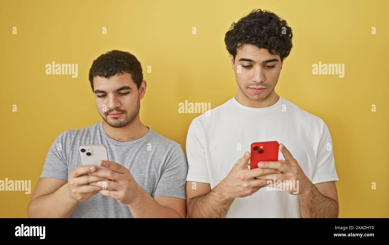 Two men using smartphones against a yellow background, portraying connectivity and casual lifestyle. Stock Photo