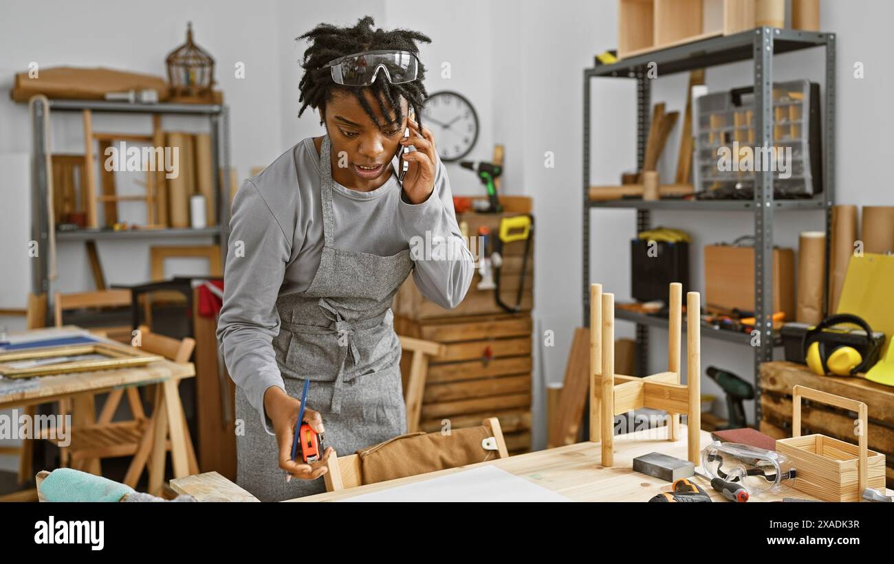 African american woman carpenter using tape measure in a woodworking workshop while talking on the phone. Stock Photo