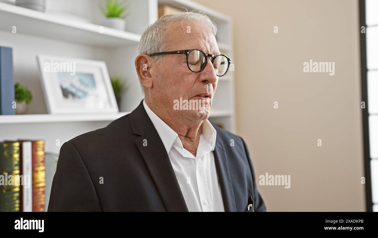 Elegant senior man boss, grey-haired and serious, stands with closed eyes, deep in focused concentration at the office workspace. Stock Photo