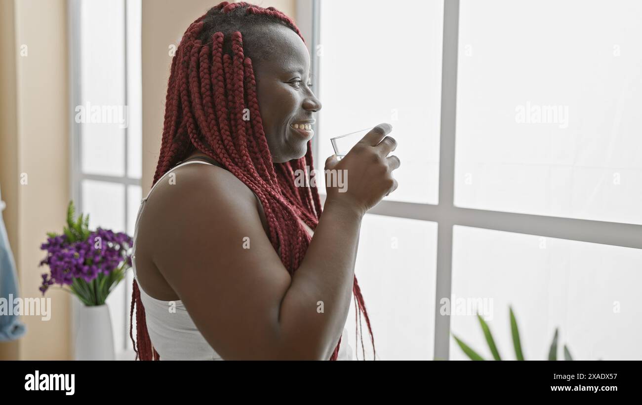 African american woman with red braids smiling indoors, holding a glass ...