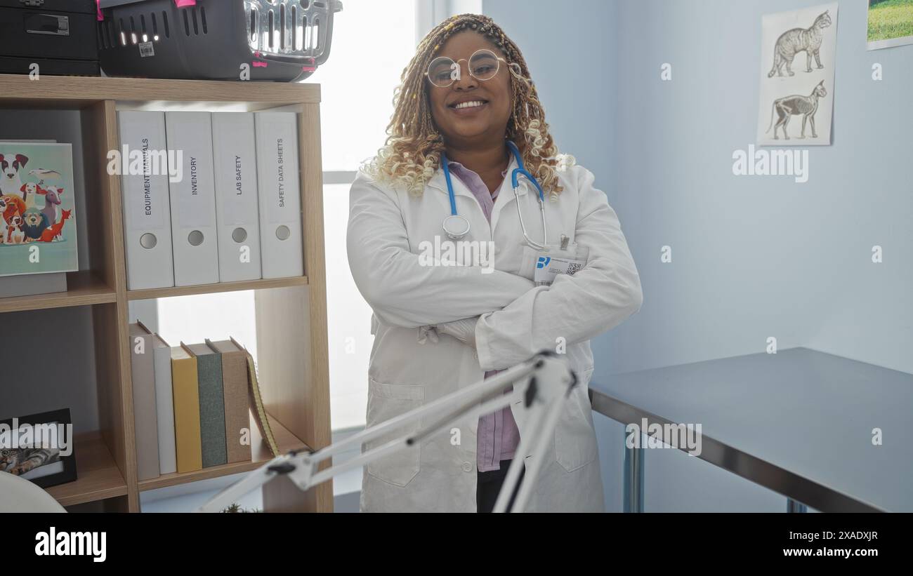 A young african american female veterinarian with braids stands confidently with crossed arms in a veterinary clinic, surrounded by medical equipment Stock Photo